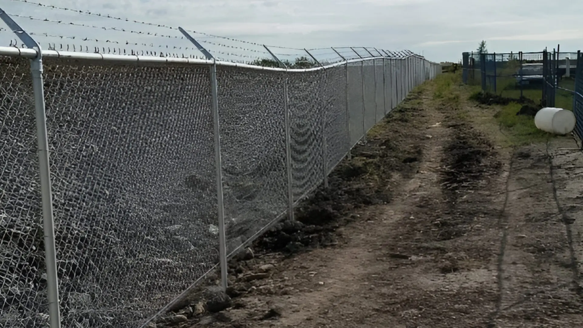 Long barbed wire fence along dirt path.