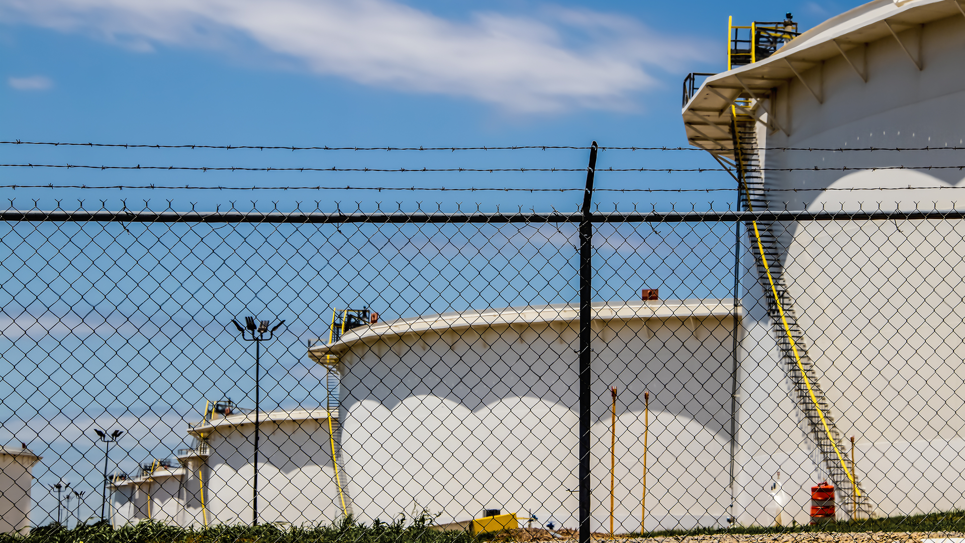 Oil storage tanks behind chain-link fence.