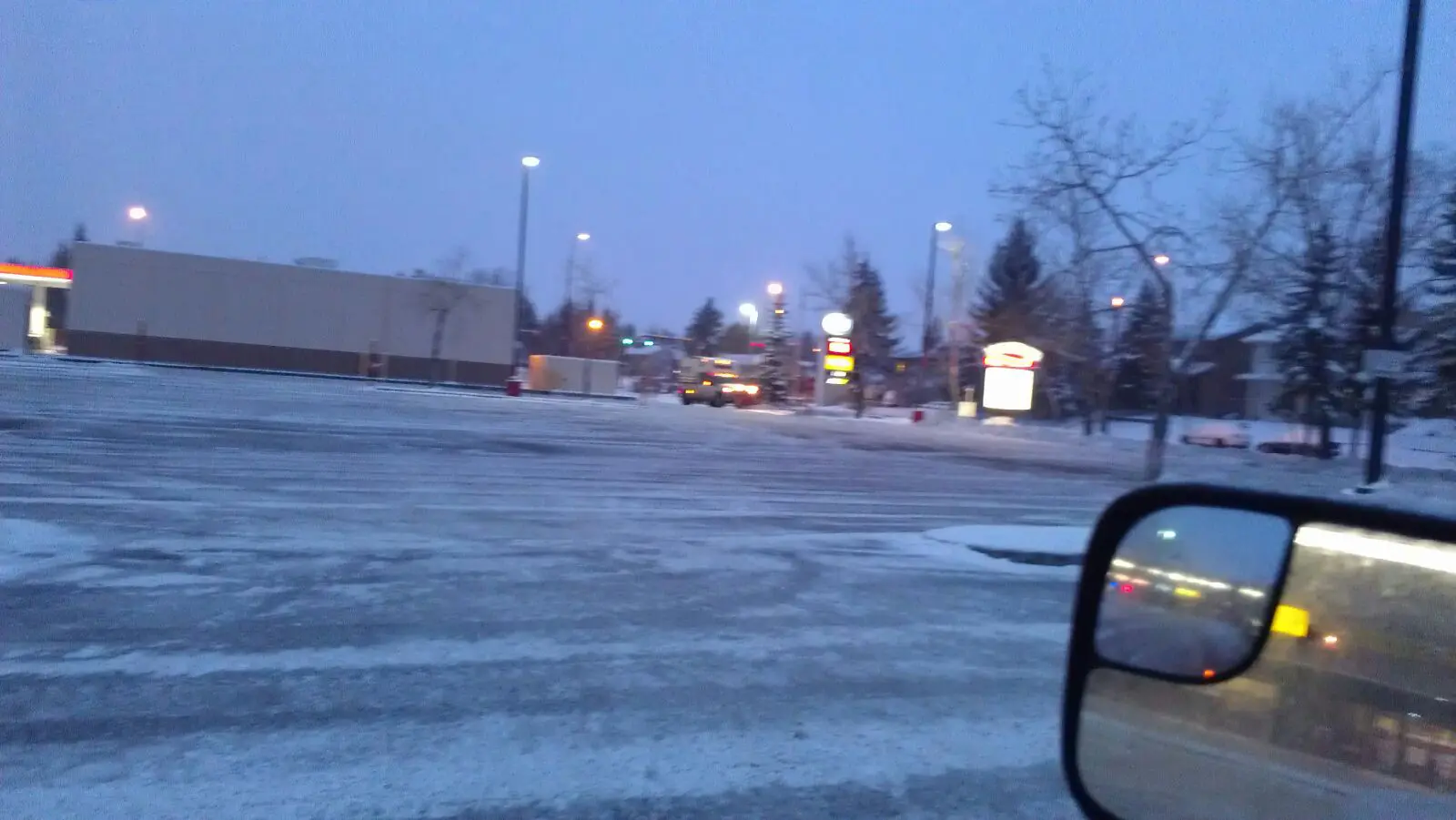 Snow-covered parking lot at dusk with streetlights on.
