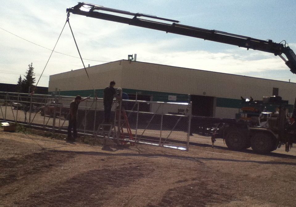 A crane lifting a metal gate near a building under construction.
