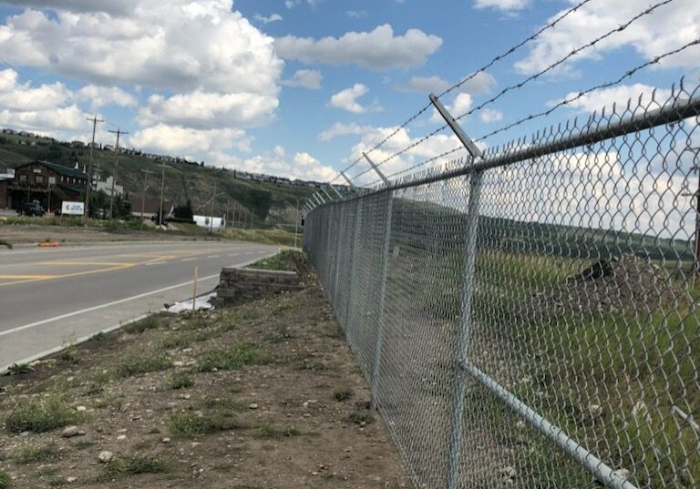 Chain-link fence topped with barbed wire along a roadside.