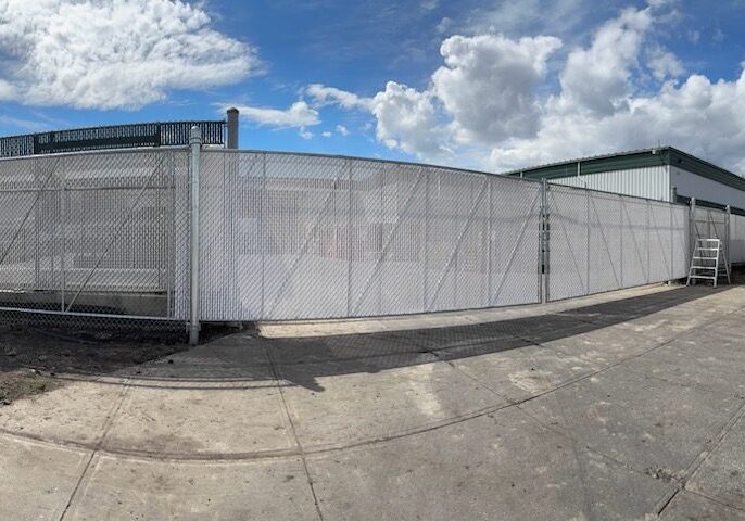 A large white metal fence with a gate under a cloudy sky.