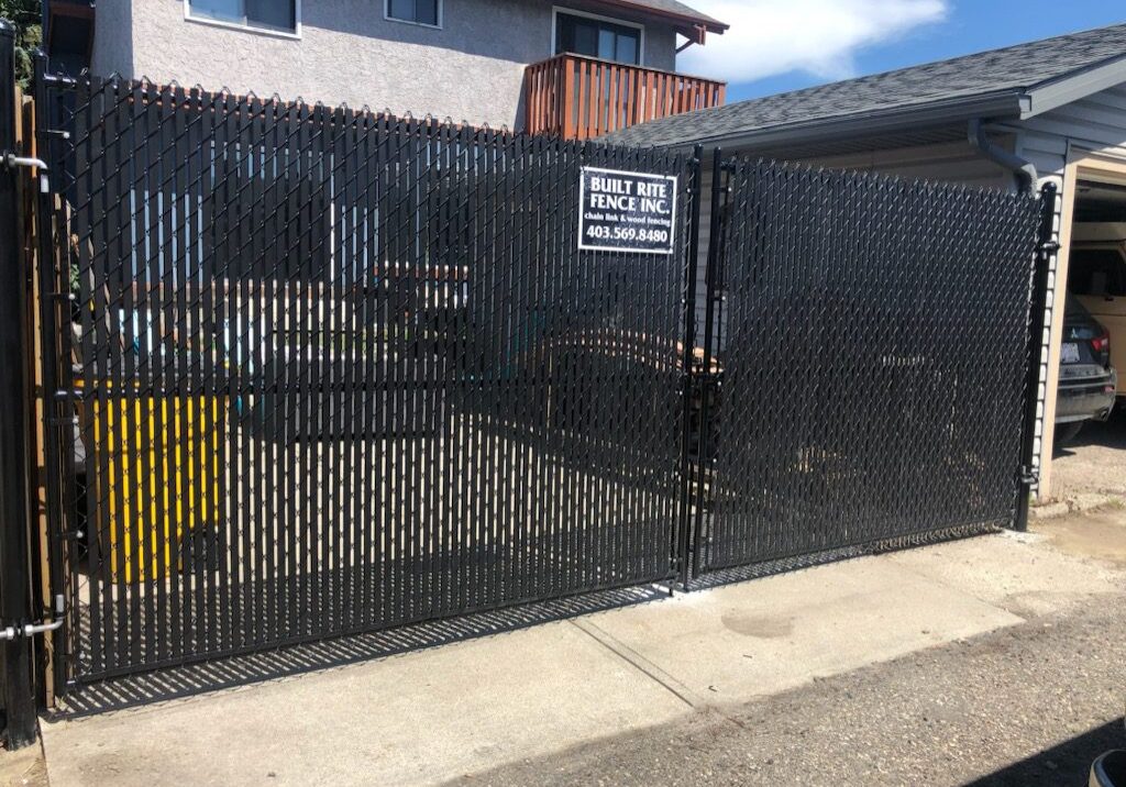 A black metal gate with a sign and a concrete pathway.