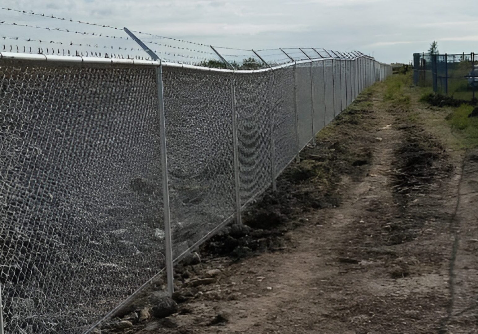 Long barbed wire fence along dirt path.